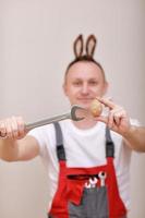 vacances de pâques, concept de célébration. un drôle d'ingénieur souriant ou un mécanicien porte des oreilles de lapin sur la tête, tenant des clés et un fond blanc d'oeuf peint. célébrer la journée orthodoxe photo