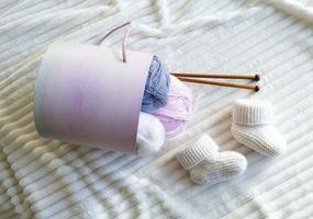 chaussons pour bébés blancs en laine tricotée et fil de laine mohair, aiguilles à tricoter. photo