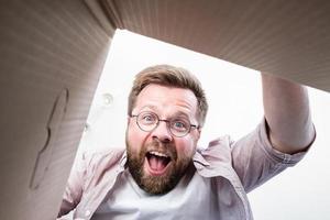 un homme à lunettes a déballé la boîte livrée avec un colis, regarde le contenu, crie de joie. déballage vue intérieure. photo