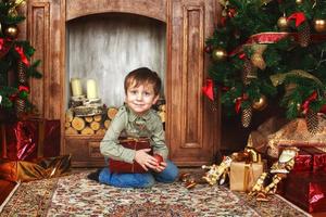 enfant garçon assis sous le sapin de noël avec boîte-cadeau photo