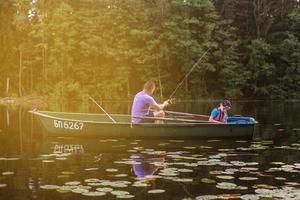 père et fils pêchant sur un lac rural au coucher du soleil sur un bateau photo