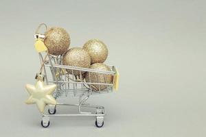 chariot de magasinage avec des boules de jouets de noël en or brillant sur fond gris photo