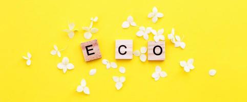 mot éco écrit à partir d'un cube en bois avec des lettres sur fond jaune avec des pétales de fleurs d'hortensia photo