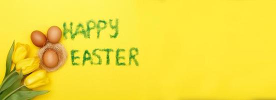 inscription joyeuses pâques d'herbe avec des oeufs de lapin, des tulipes de fleurs et un nid sur fond jaune photo