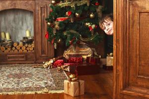 enfant garçon regarde par la porte avec une boîte-cadeau de noël. photo