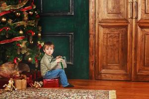 enfant garçon assis sous le sapin de noël avec boîte-cadeau photo