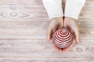 concept de noël avec main et boule blanche - jouet d'arbre de noël. boule de noël ronde blanche dans la main féminine. fond en bois photo