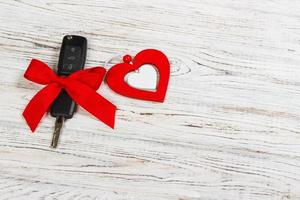 cadeau de clé de voiture de saint valentin ou de noël. clé de voiture avec un ruban rouge et un coeur sur une table en bois blanche photo