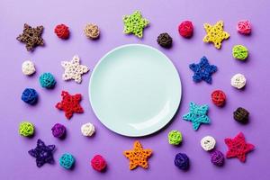 vue de dessus de l'assiette de vacances décorée de boules tricotées et d'étoiles sur fond coloré. décorations et jouets du nouvel an. concept de dîner de noël en famille photo