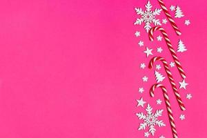 canne en bonbon de noël se trouvait uniformément dans la rangée sur fond rose avec flocon de neige décoratif et étoile. mise à plat et vue de dessus photo