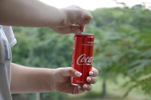 Kharkov. ukraine - 2 mai 2022 une femme caucasienne tient une boîte de conserve de coca-cola rouge avec un fond de jardin vert photo