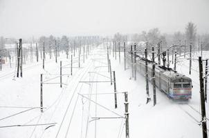 un long train de voitures voyageurs se déplace le long de la voie ferrée. paysage ferroviaire en hiver après les chutes de neige photo