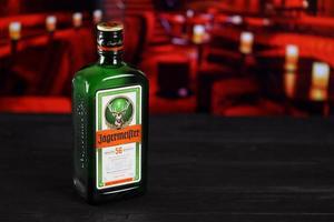 Kharkov. ukraine - 2 mai 2022 jagermeister bouteille d'élixir macéré à froid sur table en bois avec intérieur de barre rouge sur fond. alcool d'élite photo