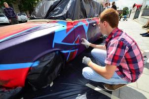 Kharkov. ukraine - 2 mai 2022 festival d'art de rue. les jeunes gars dessinent des graffitis sur la carrosserie de la voiture dans le centre-ville. le processus de dessin de graffitis de couleur sur une voiture avec des aérosols photo