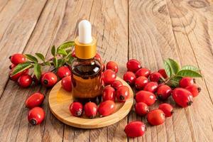 produit cosmétique de soin de la peau du visage dans une bouteille en verre avec une pipette sur une assiette en bois parmi les fruits des cynorrhodons mûrs. alimentation intensive. photo