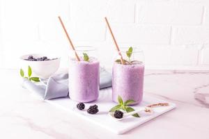 cocktail ou smoothie aux baies de mûre dans des verres en verre modernes en forme de canette de bière avec de la paille écologique en face d'un mur de briques blanches. alimentation équilibrée. photo