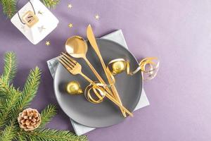 vue de dessus d'une assiette en céramique sombre avec couverts en or, décorations de noël en or sur fond gris. une copie de l'espace. photo