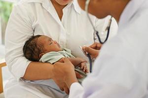 un nouveau-né garçon d'un mois métis afro-thaïlandais, visitant le médecin pour un bilan de santé avec stéthoscope à la clinique pédiatrique. consultation de concept, bilan de santé, infirmière, nourrisson en guérison. photo