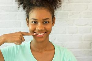 portrait headshot jeune femme afro-américaine ethnique heureuse souriante avec confiance doigt pointé positif montrant les dents blanches. concept soins de santé, dent de santé, bouche, dentaire, dentisterie, dentiste. photo