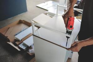 montage de meubles à la maison. déménagement pour une nouvelle maison ou un concept de bricolage. artisan utilisant un tournevis sans fil pour installer l'armoire pour installer l'armoire. photo