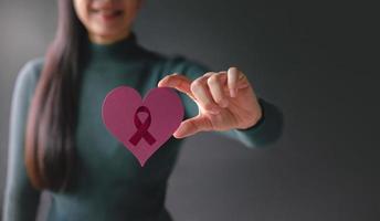 concept d'amour, de soins de santé, de cancer, de don et de charité. la sensibilisation au cancer du sein. gros plan d'une femme bénévole souriante tenant une forme de coeur avec du papier de signe de ruban de cancer photo