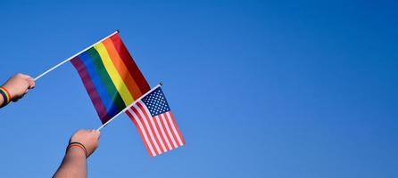 drapeau américain et drapeau arc-en-ciel levant dans les mains et contre le ciel bleu, mise au point douce et sélective, concept pour les célébrations lgbt et les événements lgbt dans le mois de la fierté aux états-unis. photo