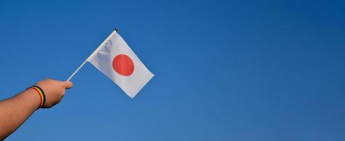 drapeau national du japon levé dans les mains et contre le ciel bleu, mise au point douce et sélective, concept pour les célébrations lgbt et les événements lgbt dans le mois de la fierté au japon photo