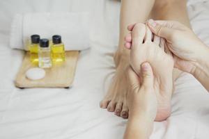 mains d'un masseur de pieds professionnel avec des huiles et des produits de soins de santé sur un lit blanc. concept de soins de santé, relaxation, traitement spa des pieds. ou introduction de produit pour le spa des pieds des femmes photo