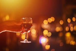 verre à vin avec du vin dans une main de femme contre des lumières défocalisées, gros plan photo