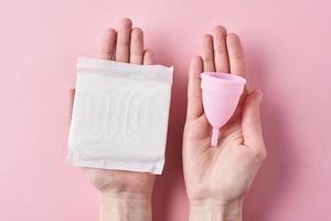 les mains d'une femme tiennent une serviette hygiénique et une coupe menstruelle sur fond rose photo