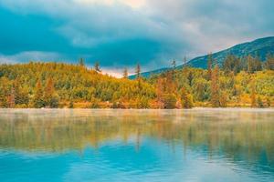 paysage de coucher de soleil d'automne avec lac de montagne paisible et tranquille. calme nature en automne. lever du soleil sur le lac brumeux avec feuillage d'automne et montagnes, ciel de nuages incroyable. feuillage de la nature fantastique photo