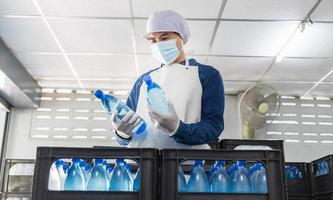 jeune homme travailleur ou inspecteur de la qualité en vêtements de travail et avec un masque de protection sur son visage travaillant à vérifier l'eau potable en bouteille dans l'usine d'eau potable avant expédition. entreprise d'eau potable photo