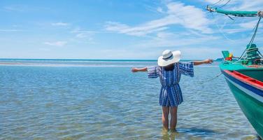 portrait d'une belle femme debout avec les bras tendus posture relaxante à côté du bateau, se détendre sur la belle plage de la mer pendant les vacances d'été. photo