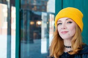 belle jeune femme aux cheveux blonds et aux yeux bleus dans un bonnet jaune sur fond de mur vert. portrait féminin de la ville. photo