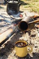 tasse en métal jaune avec café chaud et cezve sur fond de feu de joie. photo