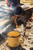 tasse en métal jaune avec café chaud et cezve sur fond de feu de joie. photo