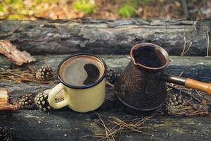 tasse en métal jaune avec café chaud et cezve sur le fond en bois avec les pièces de monnaie, les aiguilles et l'écorce d'arbre. photo