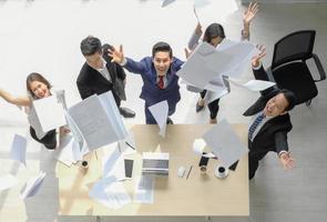 heureux groupe d'affaires exécutifs asiatiques jetant des documents pour la célébration de la réussite dans l'espace de travail de bureau, mise au point sélective, vue de dessus. photo