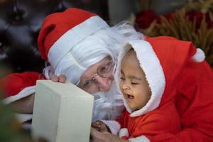 bébé afro-américain ouvre le cadeau de noël avec le père noël la nuit pour la célébration de la saison photo