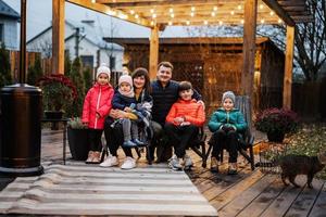 grand portrait de famille dans pergola de jardin en bois, décor lampe et chaises en automne. photo