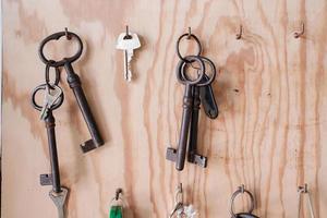 diverses clés de porte vintage et modernes sont accrochées à des crochets sur une planche de bois. photo