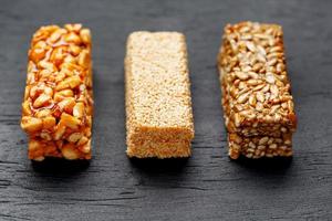 barre de granola de céréales avec cacahuètes, graines de sésame et de tournesol sur une planche à découper sur une table en pierre sombre. vue d'en-haut. trois barres assorties photo