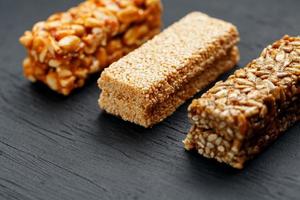 barre de granola de céréales avec cacahuètes, graines de sésame et de tournesol sur une planche à découper sur une table en pierre sombre. vue d'en-haut. trois barres assorties photo