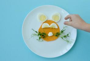 petit-déjeuner de pâques assiette de déjeuner de lapin de lapin, idée d'art culinaire amusante pour les enfants d'œufs à la coque, de crêpes et de jeunes légumes verts. vue de dessus. photo