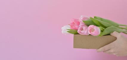 fleurs de printemps. mains tenant des tulipes roses sur une boîte. félicitation. le concept de cadeaux et de vacances de printemps photo