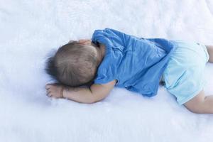 un enfant se couche sur un drap blanc dans une chemise bleue. photo