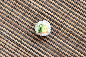 le rouleau de sushi est posé sur un tapis de couture en paille de bambou. cuisine asiatique traditionnelle. vue de dessus. minimalisme à plat tourné avec espace de copie photo