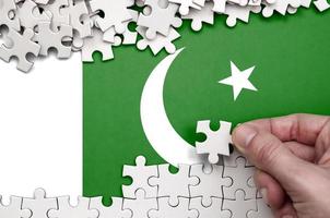 le drapeau du pakistan est représenté sur une table sur laquelle la main humaine plie un puzzle de couleur blanche photo