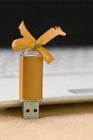 carte mémoire flash usb orange avec un arc se trouve sur une couverture de tissu polaire orange clair doux et poilu à côté d'un ordinateur portable blanc. conception de cadeau féminin classique pour une carte mémoire photo