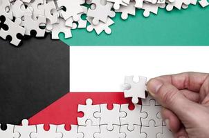 le drapeau du koweït est représenté sur une table sur laquelle la main humaine plie un puzzle de couleur blanche photo